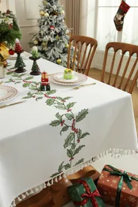 Detail van een kerstgeborduurd tafelkleed met hulstmotieven en delicate kwastjesrand.
