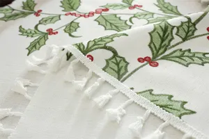 Kersttafelkleed geborduurd met feestelijke hulstbladeren, rode bessen en elegante witte kwastjes.