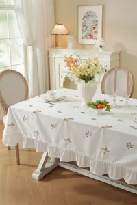 Detailed view of white cotton tablecloth with delicate floral embroidery and ruffled edge.