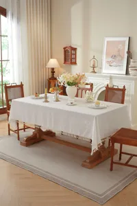 Detailansicht einer eleganten weißen Tischdecke mit Strukturmuster und zarter Fransenborte.