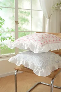 Detailed view of French style cotton pillow covers with ruffles and bows in cozy home scene.