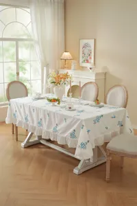 Elegant floral embroidered dining tablecloth detailed scene with delicate ruffled lace edges.