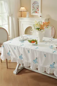 White cotton tablecloth with blue floral embroidery and ruffle hem detail, elegant home dining decor.