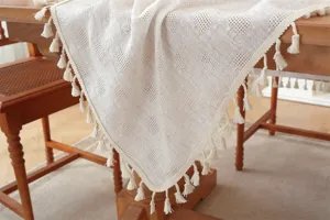 Detaillierte Nahaufnahme einer beigen Tischdecke mit kariertem Hohlmuster und Quasten.