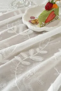 Vue détaillée d'une nappe en dentelle française blanche avec de délicats motifs de feuilles.