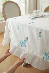 Close-up detail of white cotton tablecloth featuring blue floral embroidery and ruffled hem.