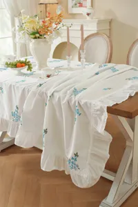 Elegant white tablecloth with blue floral embroidery and ruffle edge detail for dining table.