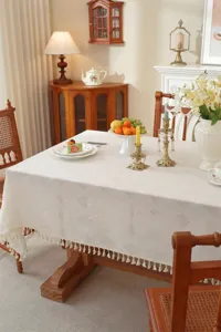 Detail einer eleganten weißen Tischdecke mit geometrischem Muster und Fransen im Esszimmer.