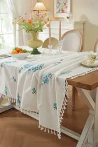 Witte katoenen tafelkleed met blauwe bloemenborduurwerk en franjes, elegante tafel.