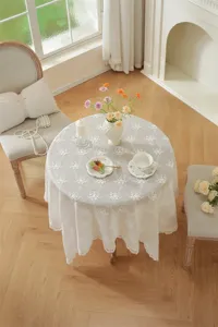 Détail de la nappe ronde blanche en dentelle avec broderie florale et tombé élégant.