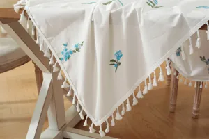 Witte katoenen tafelkleed met blauw bloemenborduurwerk en franjerand voor eetkamerdecor.