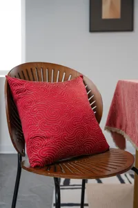 Detail shot of red jacquard pillow and tablecloth with golden pattern in cozy room setup.
