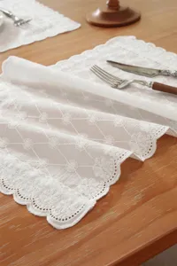 Detailaufnahme des weißen bestickten Spitzentischläufers und Tischsets auf Holztisch.