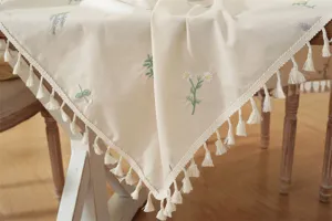 Gedetailleerd overzicht van een beige katoenen tafelkleed met fijn bloemborduursel en franjes.