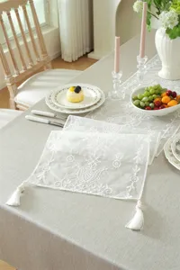 White lace table runner with floral embroidery and tassels for elegant dining room decor.