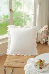 Detailed view of a white ruffle pillow cover showcased on a cozy rattan chair in a room.