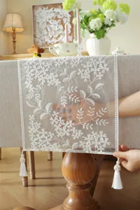 White lace table runner with floral embroidery and tassel fringe for wedding dining table decor.