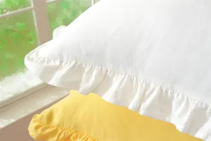 Close-up view of white cotton throw pillow cover featuring elegant ruffled edges and soft fabric.