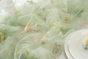 Close-up of sheer green mesh table runner with colorful floral embroidery and delicate details.