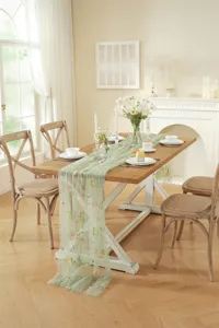 Detail view of light green mesh table runner with colorful floral embroidery and elegant pleats.