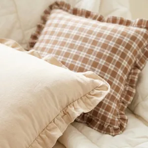Gros plan sur un coussin en coton français à carreaux caramels avec de charmants bords à volants.