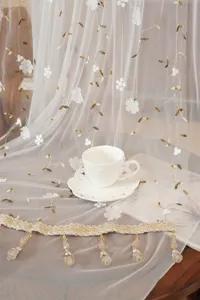 Close-up of French lace sheer curtain featuring delicate floral embroidery and beaded tassel fringe.