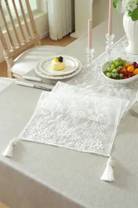 White lace table runner with floral embroidery and elegant tassels for home decoration.