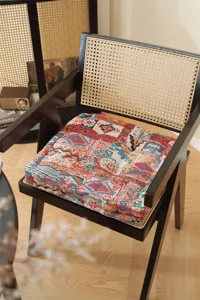 Detailed view of the colorful patchwork square seat cushion placed on a stylish woven chair.