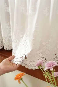 Close-up of white embroidered lace curtain detail, showing delicate floral pattern and texture.