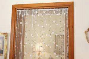 Close-up detail of sheer lace door curtain with delicate white embroidered flowers and green vines.