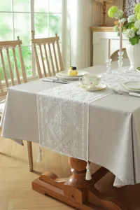 Close-up view of the white lace embroidered table runner with geometric tassels in dining setup.