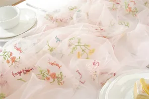 Close-up detail of pink sheer table runner with vintage floral embroidery for wedding decor.