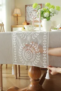 White lace table runner with floral geometric embroidery and tassels for dining and wedding decor.
