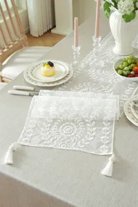 Detail view of white lace embroidered table runner with geometric floral patterns and tassels.