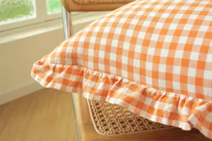 Close-up detail of orange and white plaid cotton throw pillow with delicate ruffled edge.