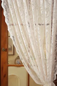 Λεπτομερής όψη γαλλικής λευκής κουρτίνας από δαντέλα ζακάρ σε ξύλινο παράθυρο κουζίνας.
