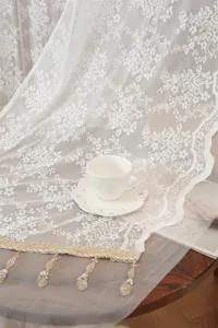 Detailed shot of French style white floral lace curtain with hanging beads on wooden table.