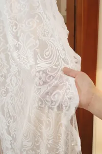 Close-up detail shot of white floral lace curtain fabric showcasing exquisite embroidery and pearl beads.