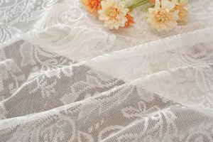 Close-up of elegant white French lace curtain fabric with delicate floral jacquard texture.