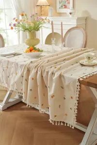 Detailopname van beige katoenen geborduurde bloementafelkleed met delicate kwastjes.
