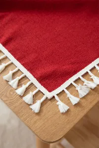 Detalle de mantel de jacquard rojo con borde de borlas blancas y textura tejida vintage.