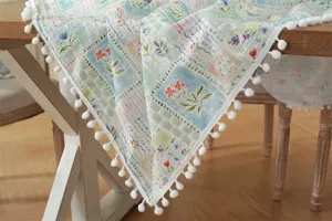 Tovaglia rettangolare in cotone stampato con graziosi pompon bianchi, dettaglio elegante.