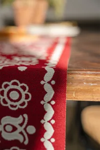 Detailed shot of a red and white jacquard table runner on a wooden table, cozy home decor.