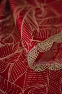 Detail view of red jacquard tablecloth featuring elegant gold lace trim and festive aesthetic.