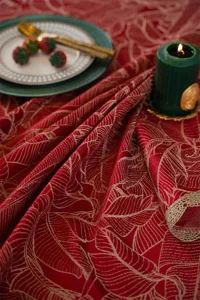 Red jacquard tablecloth detail shot with gold leaf pattern and elegant festive table decor.