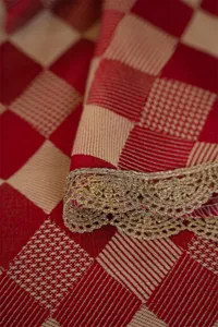 Close-up detail shot of festive red jacquard tablecloth featuring elegant metallic gold lace trim.