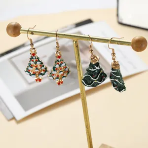 Detailed close-up view of festive Christmas tree design drop earrings on a golden stand.