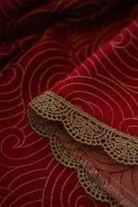 Close-up of red jacquard fabric with elegant gold lace trim for festive table decor.