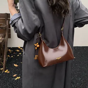 Detail view of brown patent leather hobo shoulder bag with chic wooden bead charm ornament.