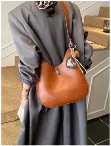 Close-up detail of stylish brown leather hobo shoulder bag with metal lock and cute charm.